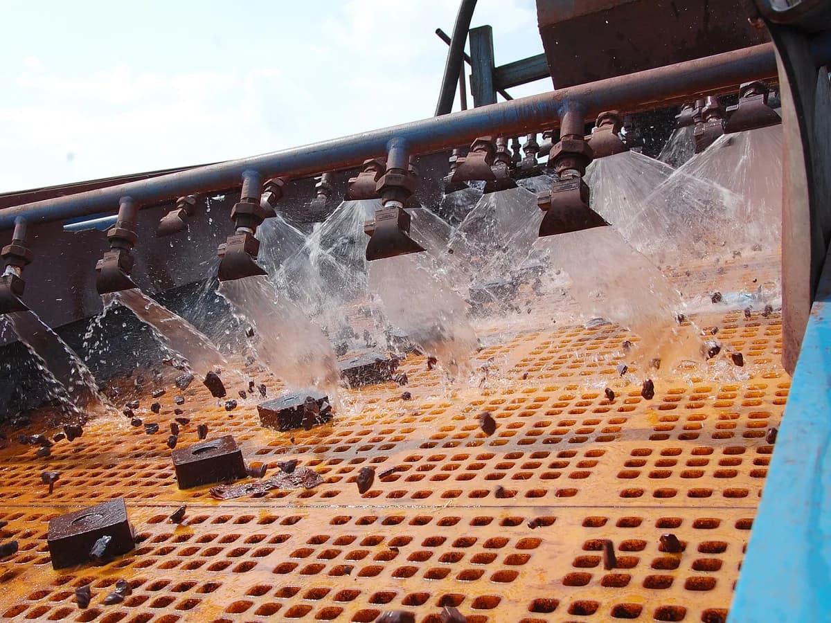 Aggregate on a vibrating screen deck under water spray nozzles (illustrative photo)